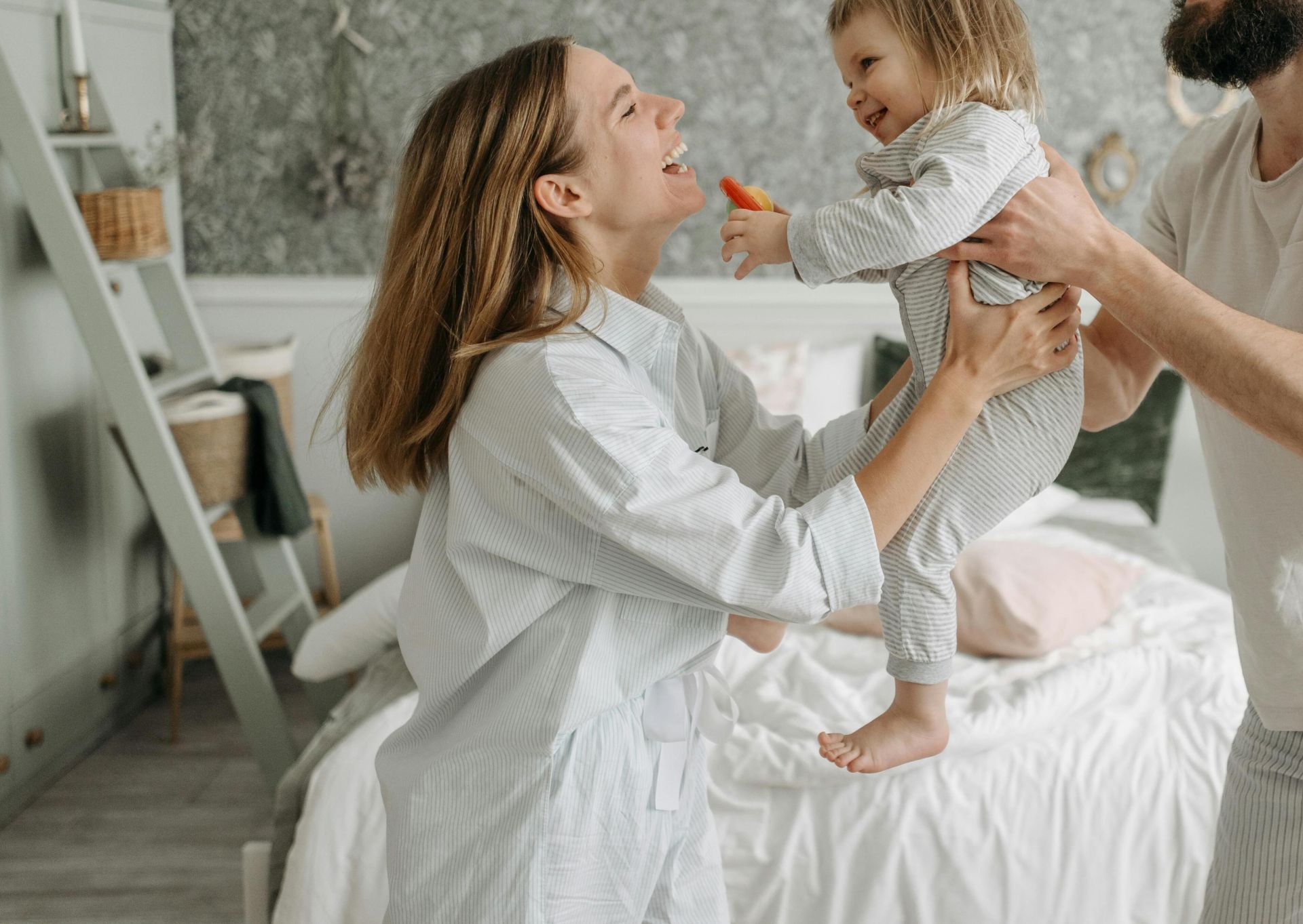 Smiling parents play with their young daughter in a bright, cozy bedroom, creating joyful family memories.